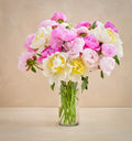 Bouquet of pink, white, and yellow flowers in a clear vase on a beige background