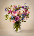 Bouquet of pink, white, and blue flowers in a clear vase on a beige background