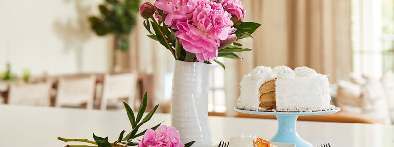Pink peonies arranged in a white vase on a table with cake
