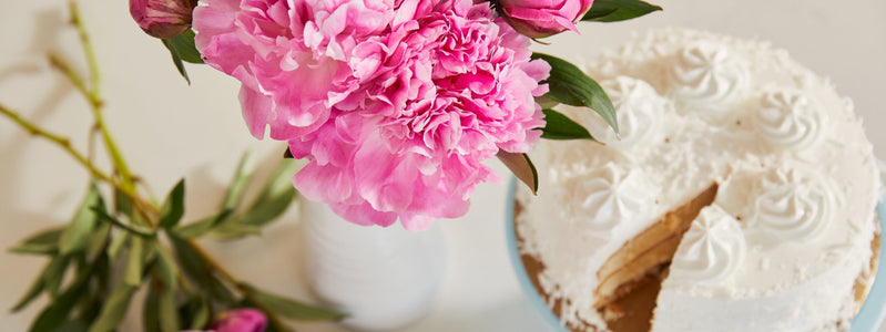 Bouquet of bright pink peonies on a table with frosted white birthday cake.