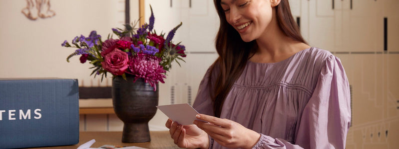 Close up of a woman sitting at a table reading a card next to her UrbanStems arrangement.
