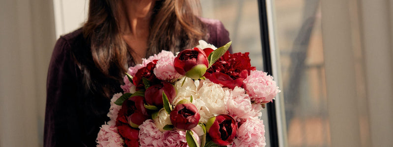 Close up of a woman smiling while holding a bouquet of peony flowers.