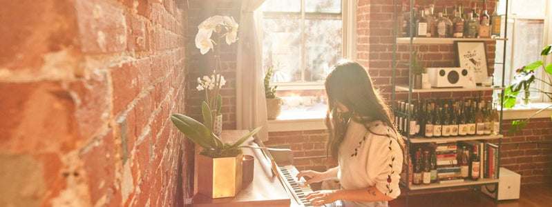 Woman playing piano in the sunlight with two white orchid flowers