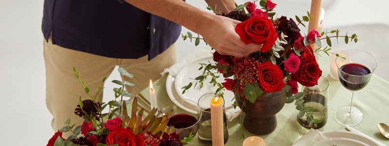 Close up of a man arranging red roses on the dining room table for Valentine's Day.