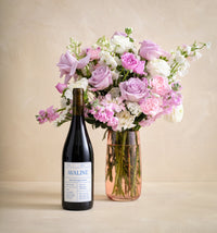 Bottle of Avaline wine with a bouquet of pink and white flowers in a clear vase on a beige background