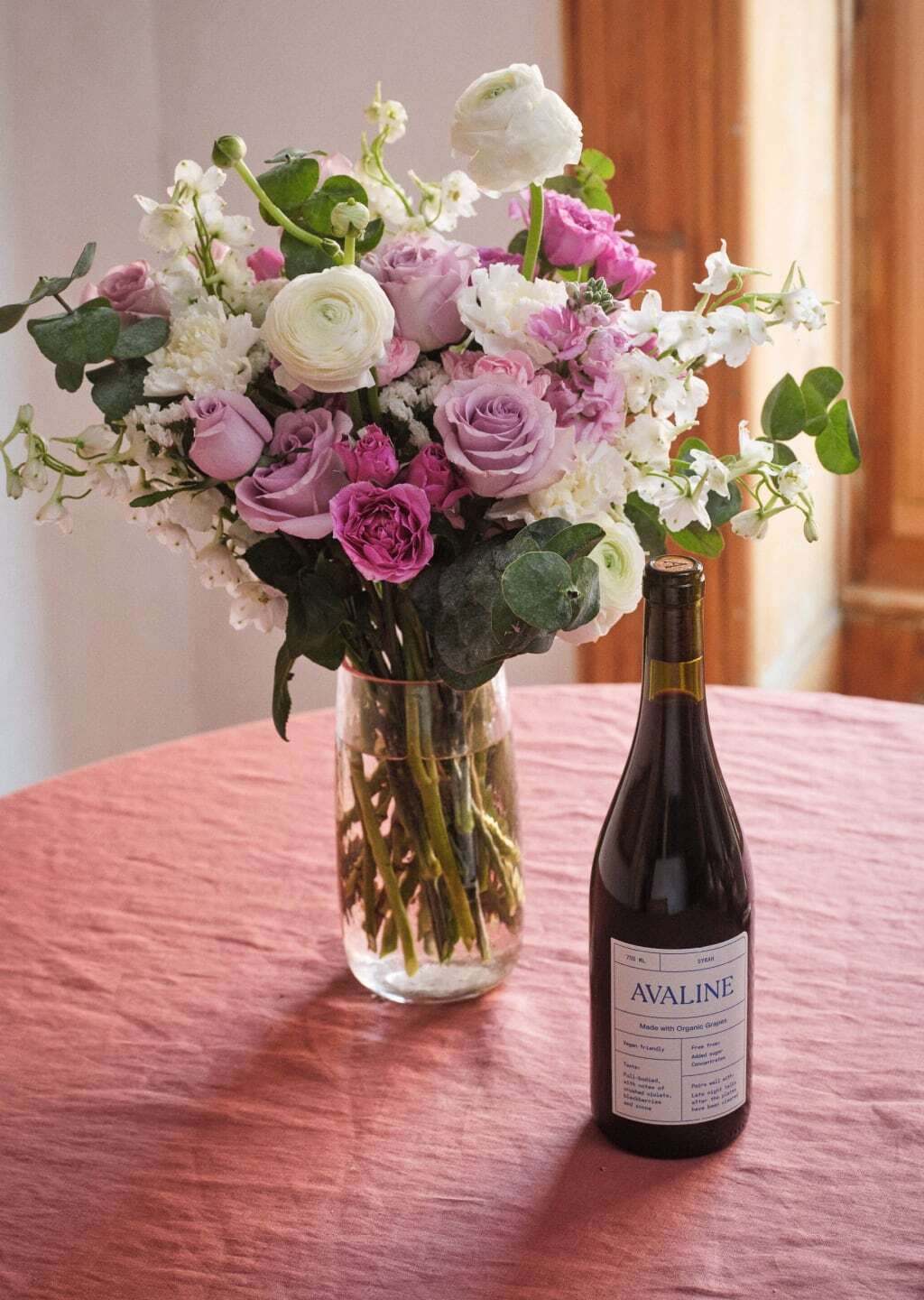 Bouquet of flowers in a vase next to a bottle of Avaline wine on a wooden table.