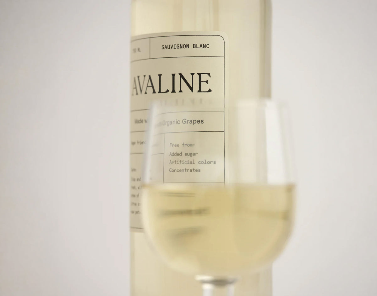 Avaline Sauvignon Blanc wine bottle with a glass of white wine on a light background