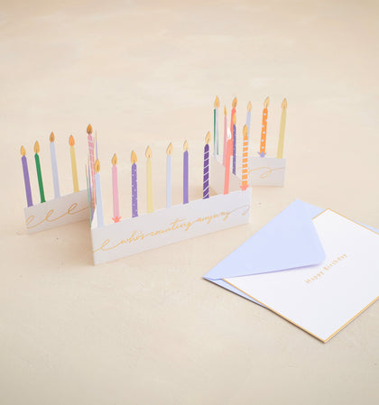 Greeting card with colorful candles and an envelope on a beige background