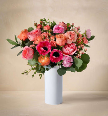 Bouquet of pink, orange, and red flowers in a white vase on a beige background