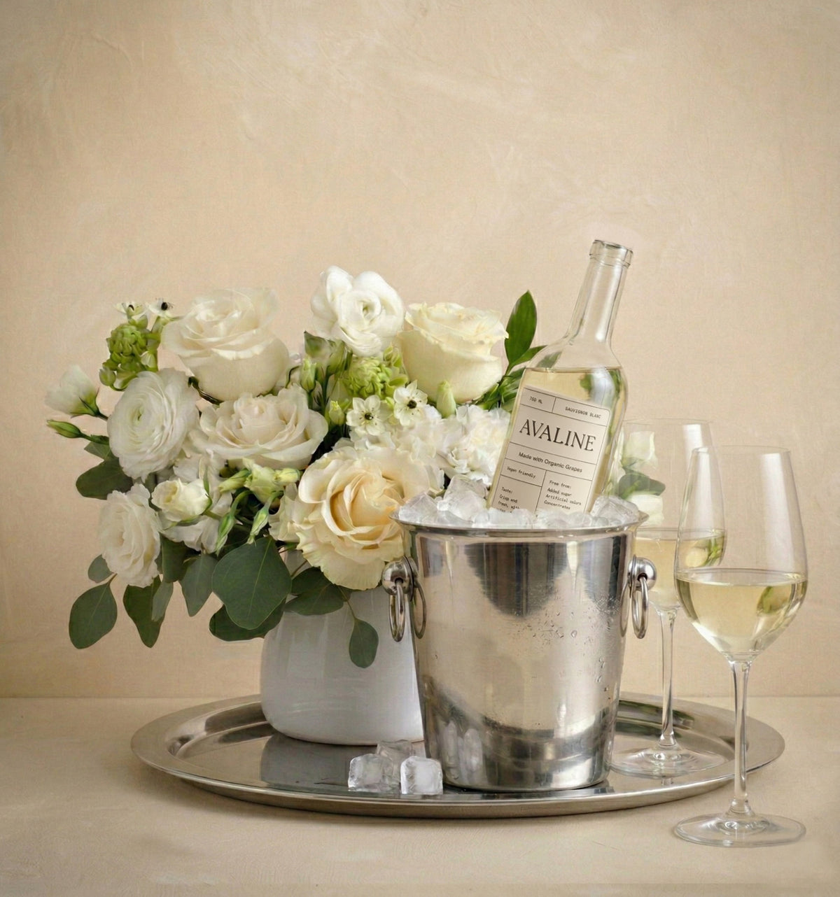 Wine bottle in an ice bucket with a bouquet of flowers on a tray, against a beige background