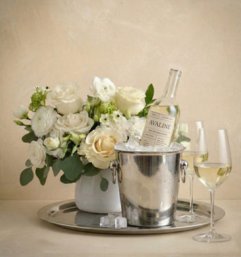 Wine bottle in an ice bucket with a bouquet of flowers on a tray, against a beige background