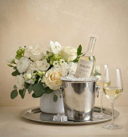 Wine bottle in an ice bucket with a bouquet of flowers on a tray, against a beige background