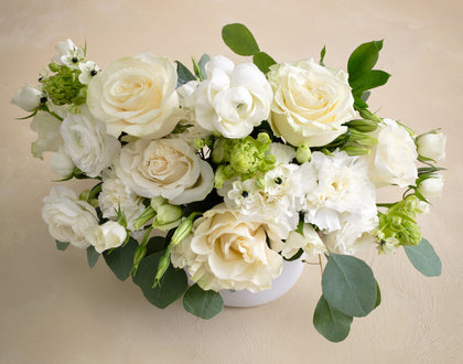 Bouquet of white and green flowers in a white vase on a beige background