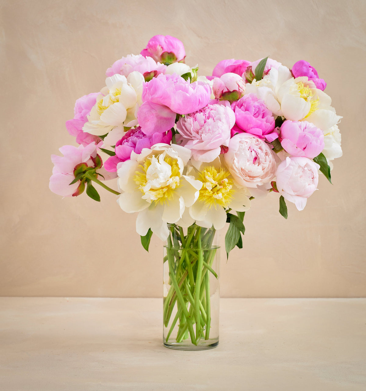 Bouquet of pink, white, and yellow flowers in a clear vase on a beige background