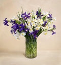 Bouquet of purple and white flowers in a clear vase on a beige background