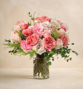 Bouquet of pink and white roses in a clear vase on a beige background