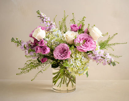Bouquet of pink, white, and green flowers in a clear vase on a beige background