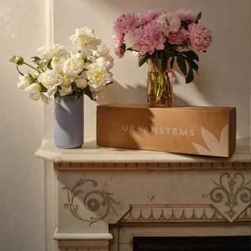 Two vases with flowers on a decorative fireplace mantle, featuring UrbanStems branding.
