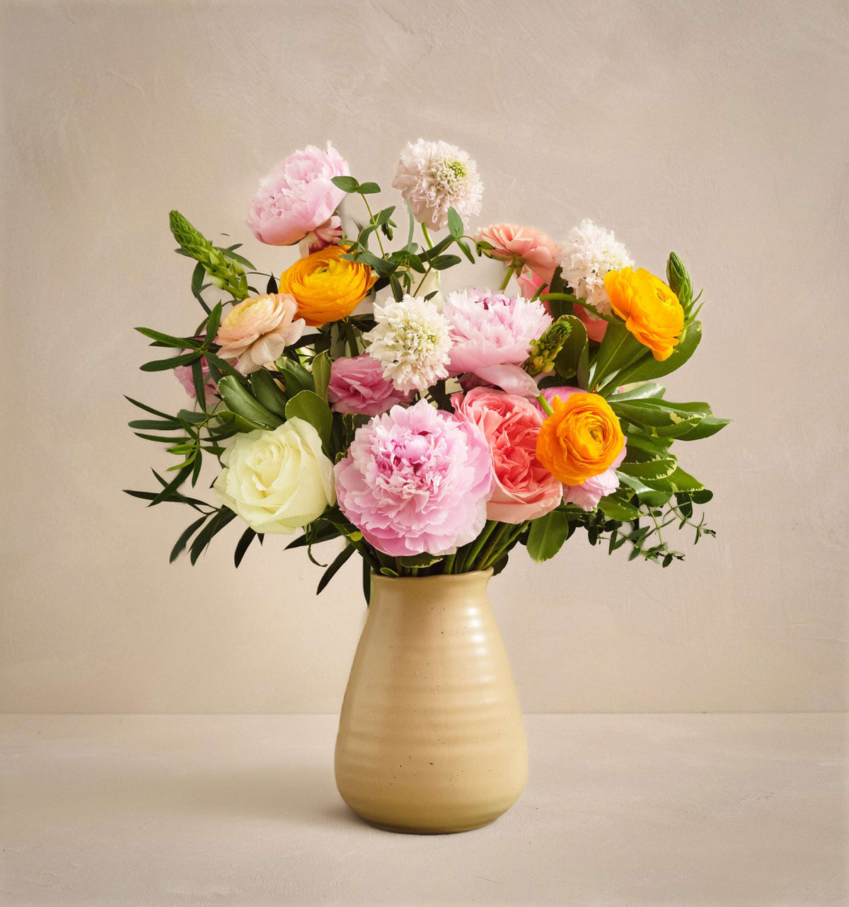 Bouquet of colorful flowers in a beige vase on a neutral background