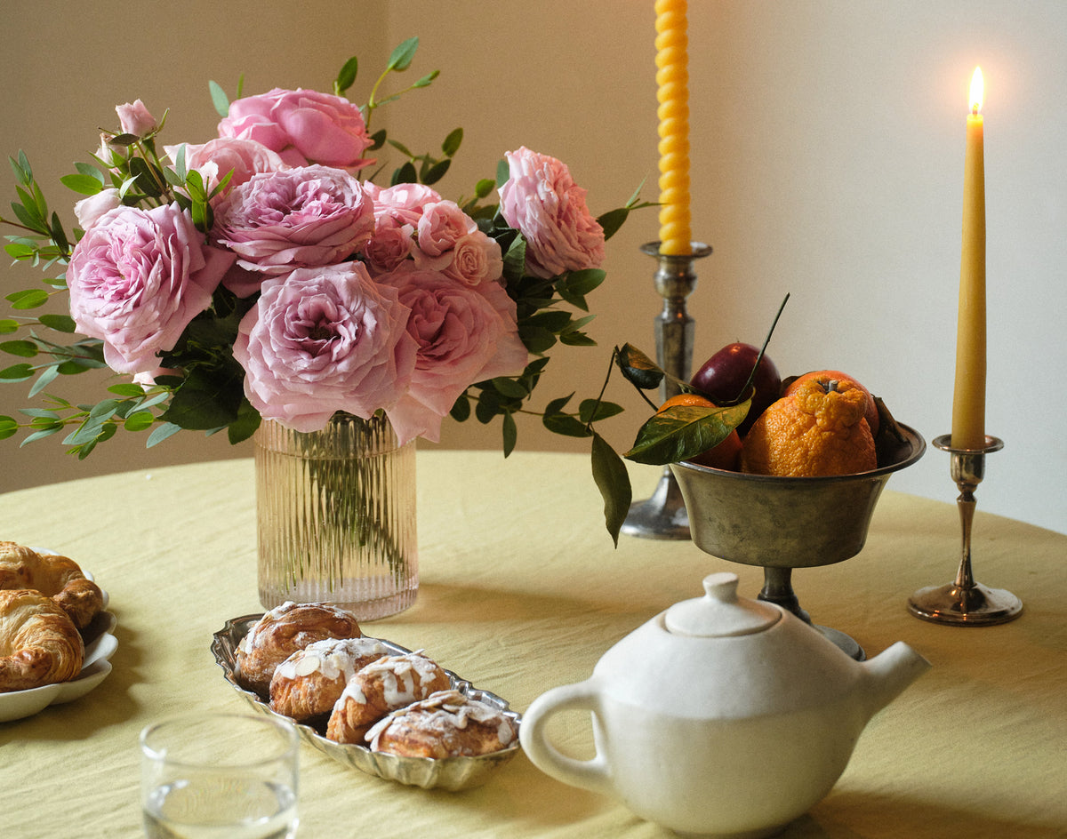Table setting with pink roses, pastries, a teapot, and candles.