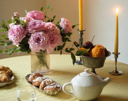 Table setting with pink roses, pastries, a teapot, and candles.