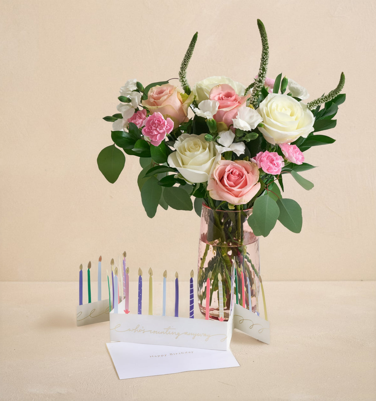 Bouquet of flowers in a clear vase with birthday candles and a card on a beige background