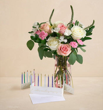 Bouquet of flowers in a clear vase with birthday candles and a card on a beige background