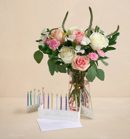Bouquet of flowers in a clear vase with birthday candles and a card on a beige background