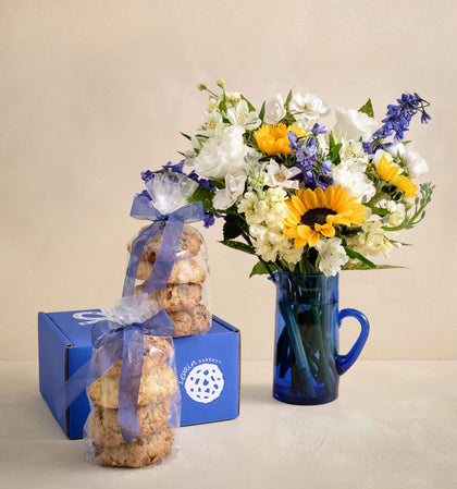 Bouquet of flowers in a blue mug and stacked cookies with a blue box on a beige background