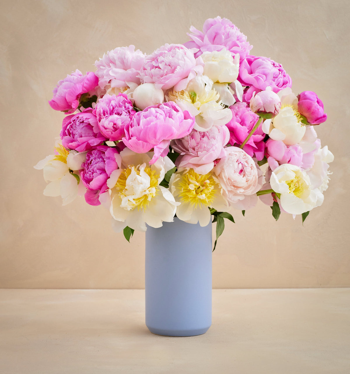Bouquet of pink, white, and yellow flowers in a light blue vase on a beige background