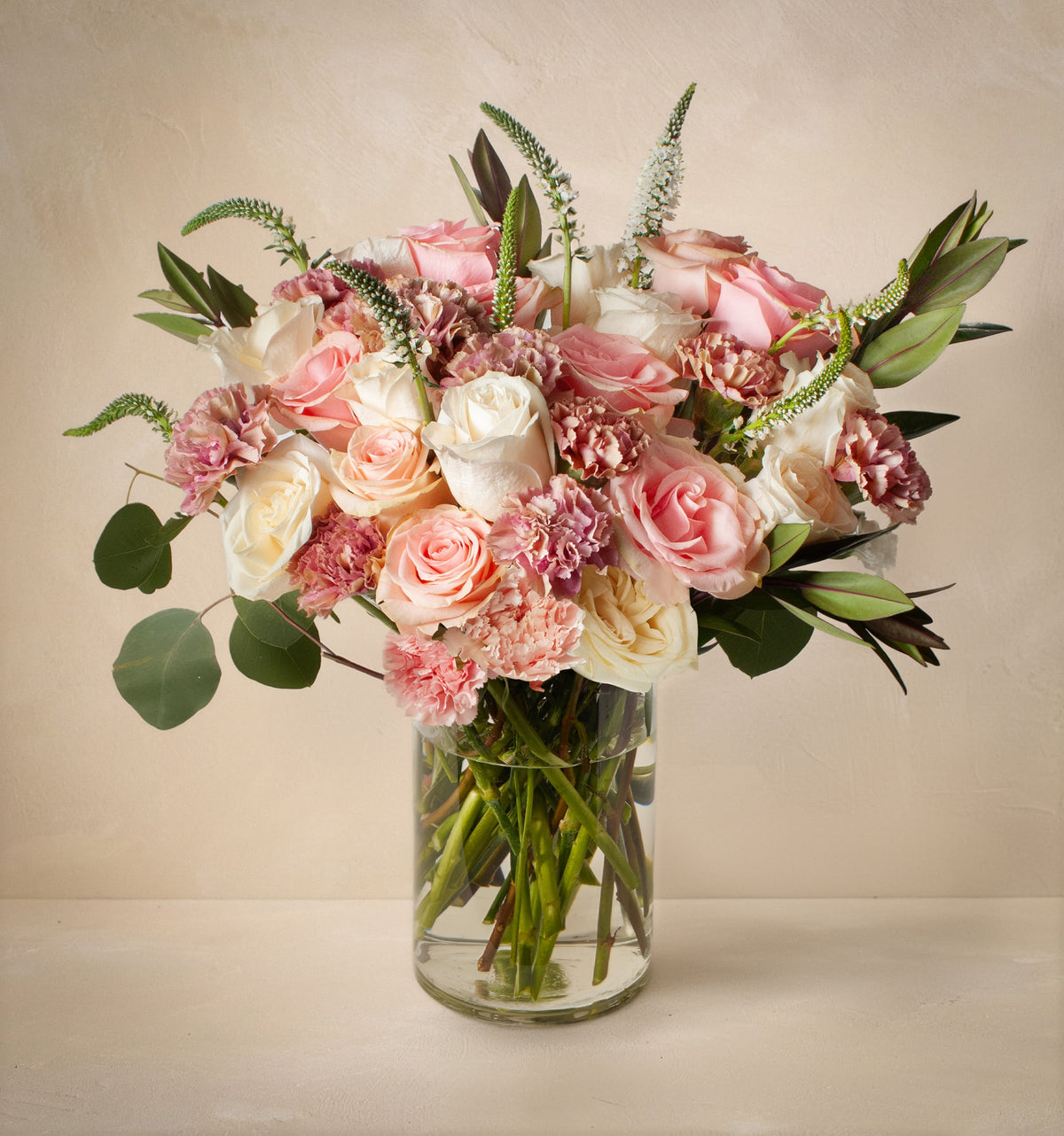 Bouquet of pink and white flowers in a clear vase on a beige background