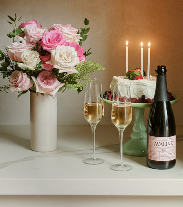 Wine bottle, glasses, cake with candles, and flowers on a table.